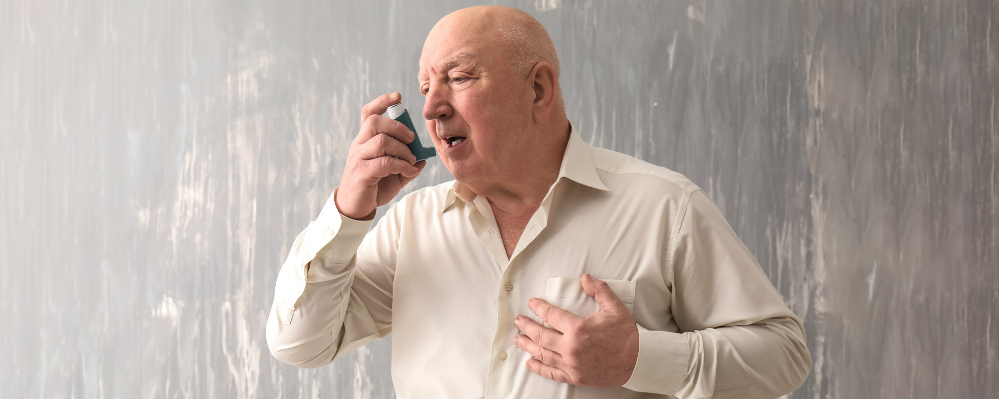 senior man with inhaler having asthma attack on grey background